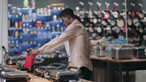 Young Afroamerican Married Couple is Choosing Electric Waffle Iron or Grill in Home Appliances Store alt