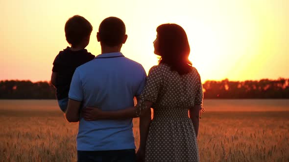 The Family Stands in a Wheat Field and Enjoys the Sunset. A Man Father Holds His Son in His Arms, a alt