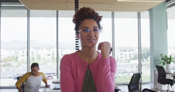 Portrait of smiling biracial creative businesswoman in office with diverse colleagues in background alt
