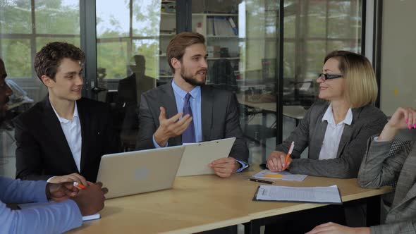 Businessman in Suit Talking to Businesspeople Colleagues Sitting at the Table alt