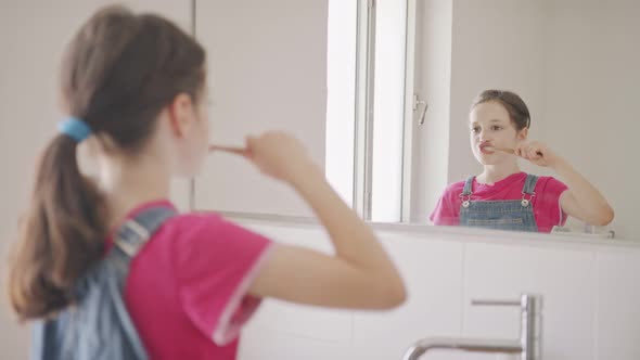 Little girl brushing her teeth in the bathroom in the morning alt