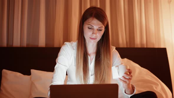 Young Woman Drinking Coffee and Using Laptop at Hotel Room alt