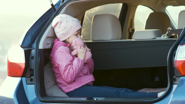 Pretty Happy Child Girl Playing with a Pink Toy Teddy Bear in a Car Trunk alt