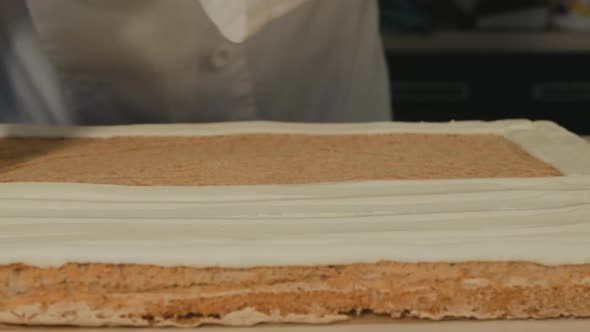 Pastry Chef Squeezes Butter Cream Out of the Cooler Onto a Sponge Cake for a Meringue Roll alt