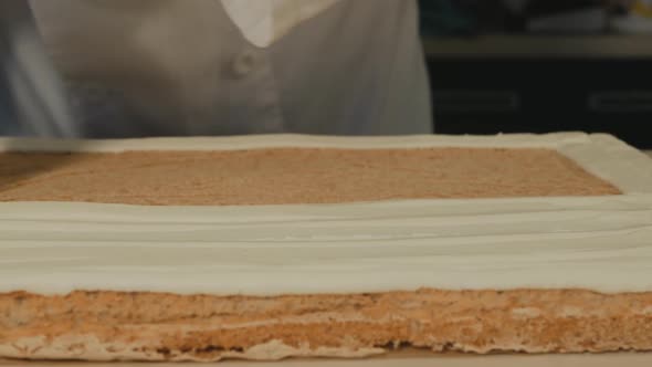 Pastry Chef Squeezes Butter Cream Out of the Cooler Onto a Sponge Cake for a Meringue Roll