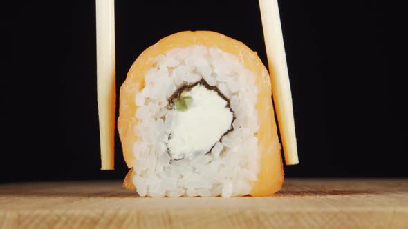 Human hand takes a sushi by chopsticks from a wooden plate