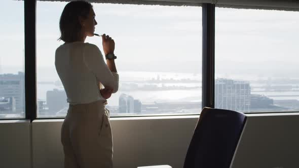 Back view of caucasian businesswoman standing at window and thinking alt