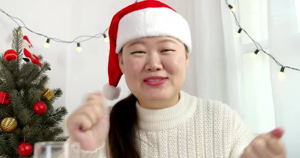 Asian woman wearing hat having video call drinking and celebrating Christmas online