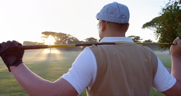 Golfer carrying golf club over shoulder while standing on the golf course alt