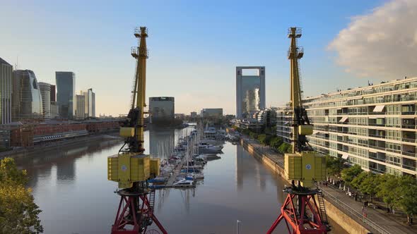 Aerial flying between two old port cranes towards boats docked in Puerto Madero at golden hour alt