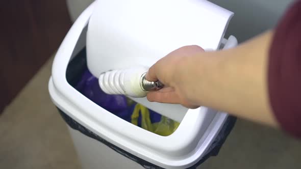 A woman throws broken fluorescent light bulb in a regular trash bin. Improper disposal electronics alt