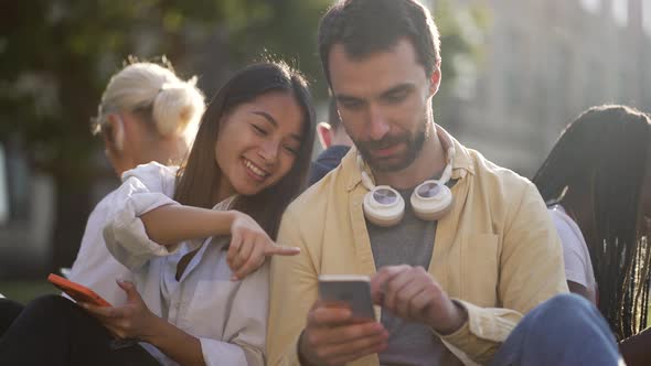 Busy on Phones Diverse Students Sitting on Lawn alt