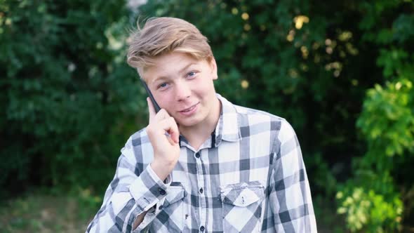 Young Caucasian Teenager Man in a Light Gray Checkered Shirt Speaks on the Phone alt