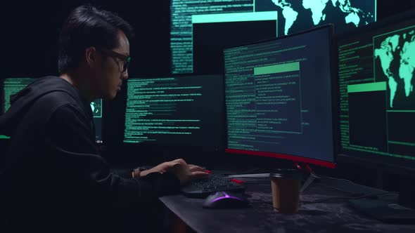 Asian Male Hacker Hacking With Multiple Computer Screens In Dark Room alt