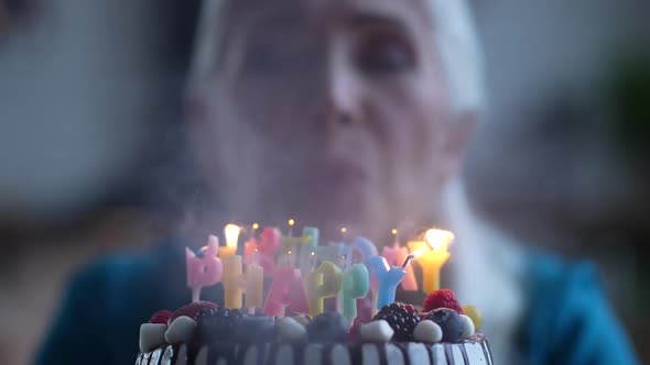 Happy Old Lady Blowing Candles on Birthday Cake alt