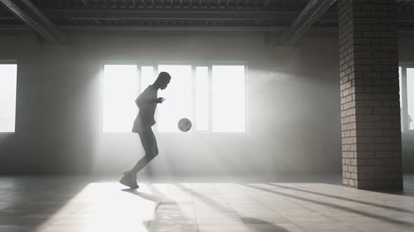A Black Guy Trains with a Soccer Ball in an Underground Parking Lot in the Sunlight in Slow Motion alt