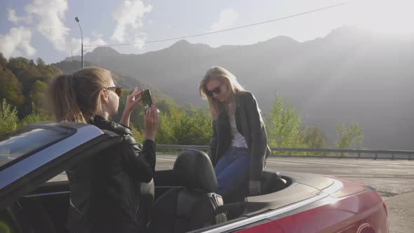 Two Caucasian Girls in a Cabriolet are Photographed on a Smartphone and Smiling