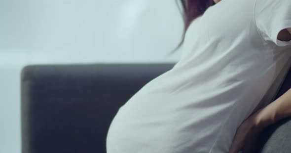 Young Asian Pregnant woman sitting on a sofa in the living room at home.