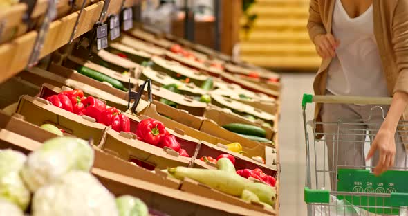 Closeup a Woman Takes Vegetables From a Shelf in a Supermarket and Puts Them in a Bag