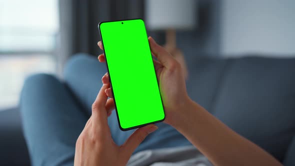 Woman at Home Lying on a Sofa and Using Smartphone with Green Mock-up Screen in Vertical Mode. Girl alt