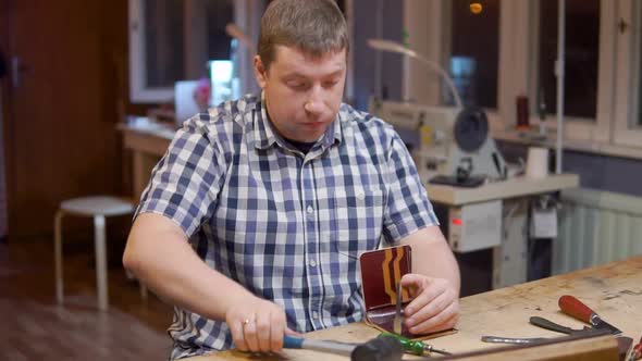 Master of Creating Handmade Leather Wallets Beats a Hammer on the Tool That Makes Holes in the