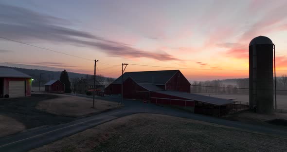 Colorful sunrise and morning mist. Aerial establishing shot of rural farm scene in USA. Barn and sil alt