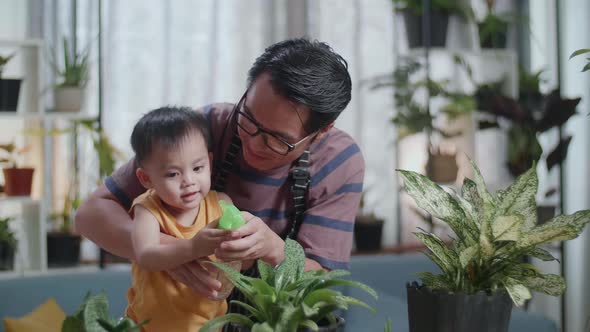 Happy Asian Man With Son Watering Plants At Home alt
