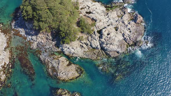 Rocky Island Washed By Waves Covered with Coniferous Trees in a Sea Bay alt