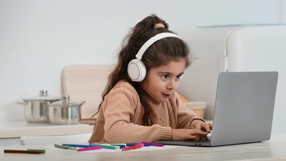 Little Girl Using Laptop Playing Games Wearing Headphones At Home alt