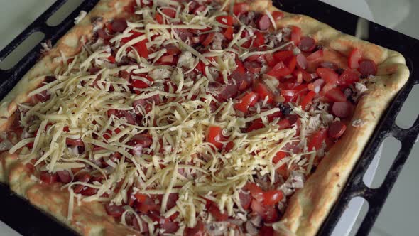 Housewife throws grated cheese on cooked pizza on oven tray