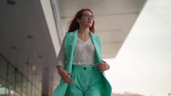 Beautiful confident business woman in glasses and a turquoise fashionable suit walks. Slow motion alt
