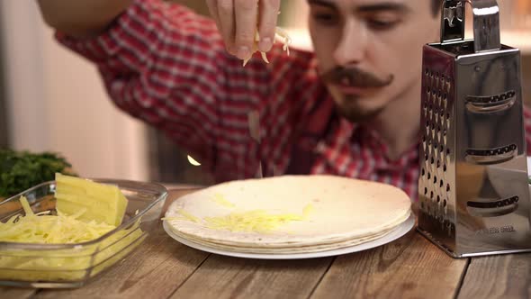 Closeup Footage of a Cook Who is Throwing Grated Cheese on Tortilla Lying on a Plate on Wooden Table alt