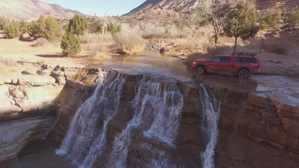 Flying over truck driving through river at the top of a waterfall alt