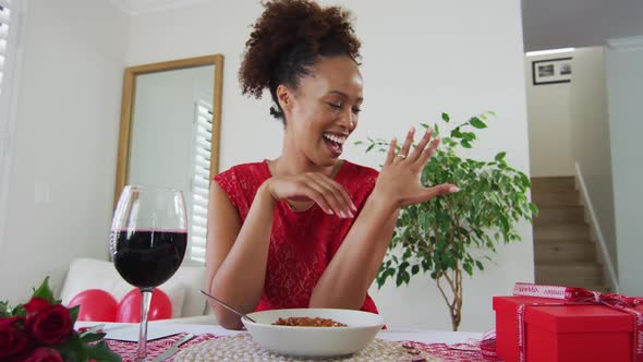 Happy mixed race woman on a valentines date video call, drinking wine alt