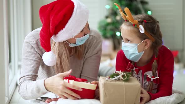 Mom and daughter in medical masks exchange gifts under the New Year's tree