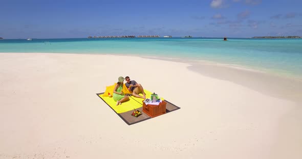 Aerial drone view of a man and woman couple having a picnic meal on a tropical island beach alt