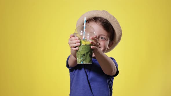 Cute boy Drinking Mojito cocktail From Plastic Cup Over Yellow Studio Background alt