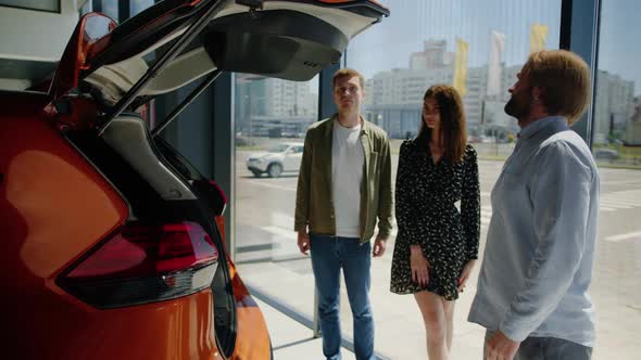 The Manager Shows a Young Couple a Car at a Dealership alt