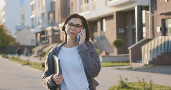 Smiling Young Caucasian Woman in Glasses Holding Laptop During Walking Talking with Best Friend alt