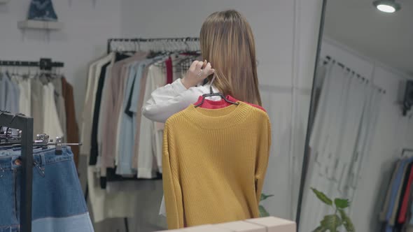 Slim Confident Woman Hanging Sweaters on Shoulder Turning Looking Back alt