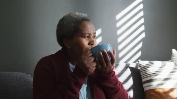 Thoughtful african american senior woman drinking coffee, looking into distance alt