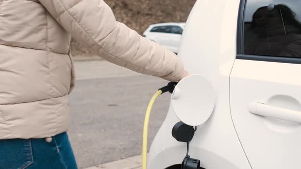 Woman Coming to the Electric Vehicle and Unplugging Power Supply Cable to Charge in the Street at alt