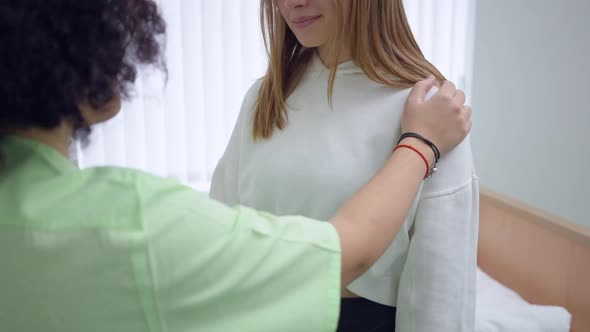 Unrecognizable Ill Woman Standing in Hospital with Doctor Nurse Tapping Shoulder Supporting Lady alt