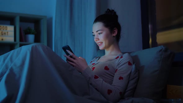 Teenage Girl in Pajamas with Phone in Bed at Night alt