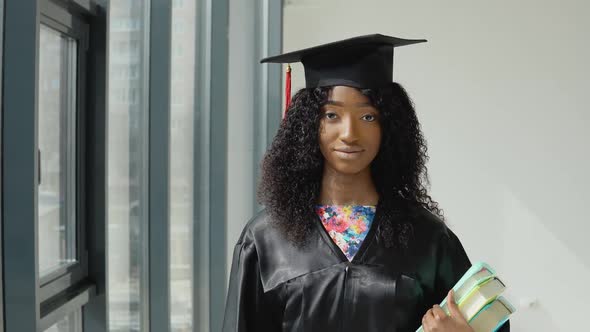 Young African American Female University Graduate Standing with Textbooks in Hands Near a Large alt