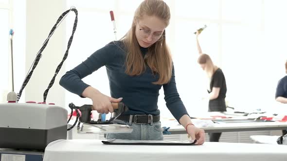 employee of a clothing factory smoothes her sewn clothes with a steam iron alt