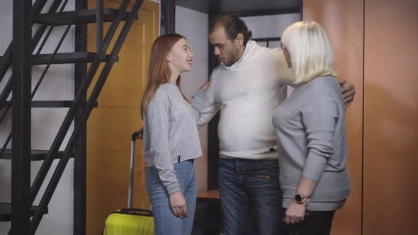 Reunion of Happy Caucasian Family After Trip. Cheerful Smiling Man Hugging Joyful Wife and Daughter alt