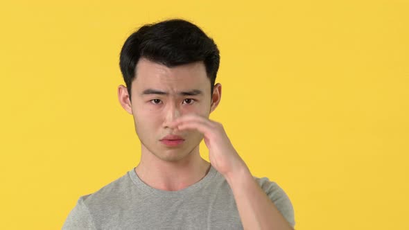 Sad Asian young man crying isolated on yellow background