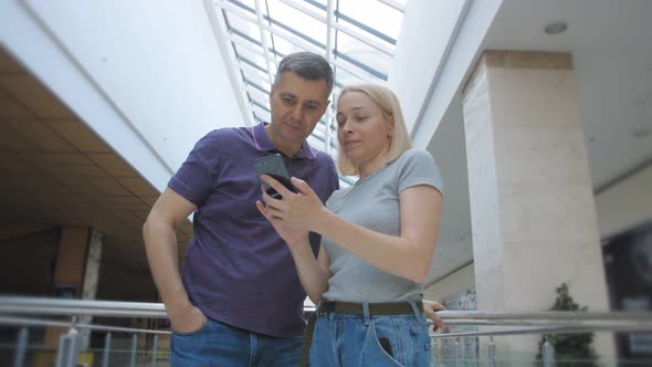 A Man and a Woman Keen Look at the Smartphone Screen and About Something Talk alt