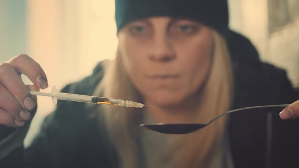 Woman with Syringe and Spoon Preparing Dose of Narcotics alt